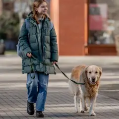 Ragazza sorridente passeggia con il suo cane al guinzaglio su un marciapiede lastricato.