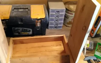 Costruzione di una mangiatoia per galline fai da te. In primo piano, una struttura in legno grezzo. Sullo sfondo, una cassetta degli attrezzi, contenitori a cassetti e una livella.