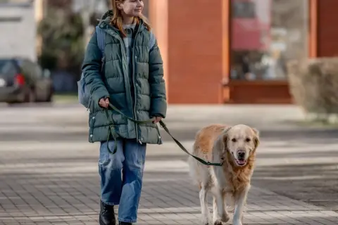 Ragazza sorridente passeggia con il suo cane al guinzaglio su un marciapiede lastricato.