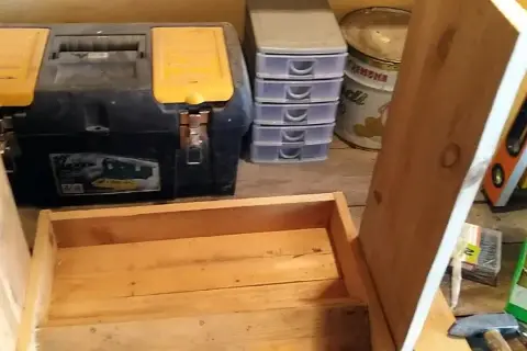 Costruzione di una mangiatoia per galline fai da te. In primo piano, una struttura in legno grezzo. Sullo sfondo, una cassetta degli attrezzi, contenitori a cassetti e una livella.