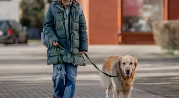 Ragazza sorridente passeggia con il suo cane al guinzaglio su un marciapiede lastricato.