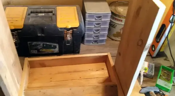 Costruzione di una mangiatoia per galline fai da te. In primo piano, una struttura in legno grezzo. Sullo sfondo, una cassetta degli attrezzi, contenitori a cassetti e una livella.