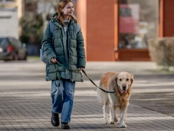 Ragazza sorridente passeggia con il suo cane al guinzaglio su un marciapiede lastricato.